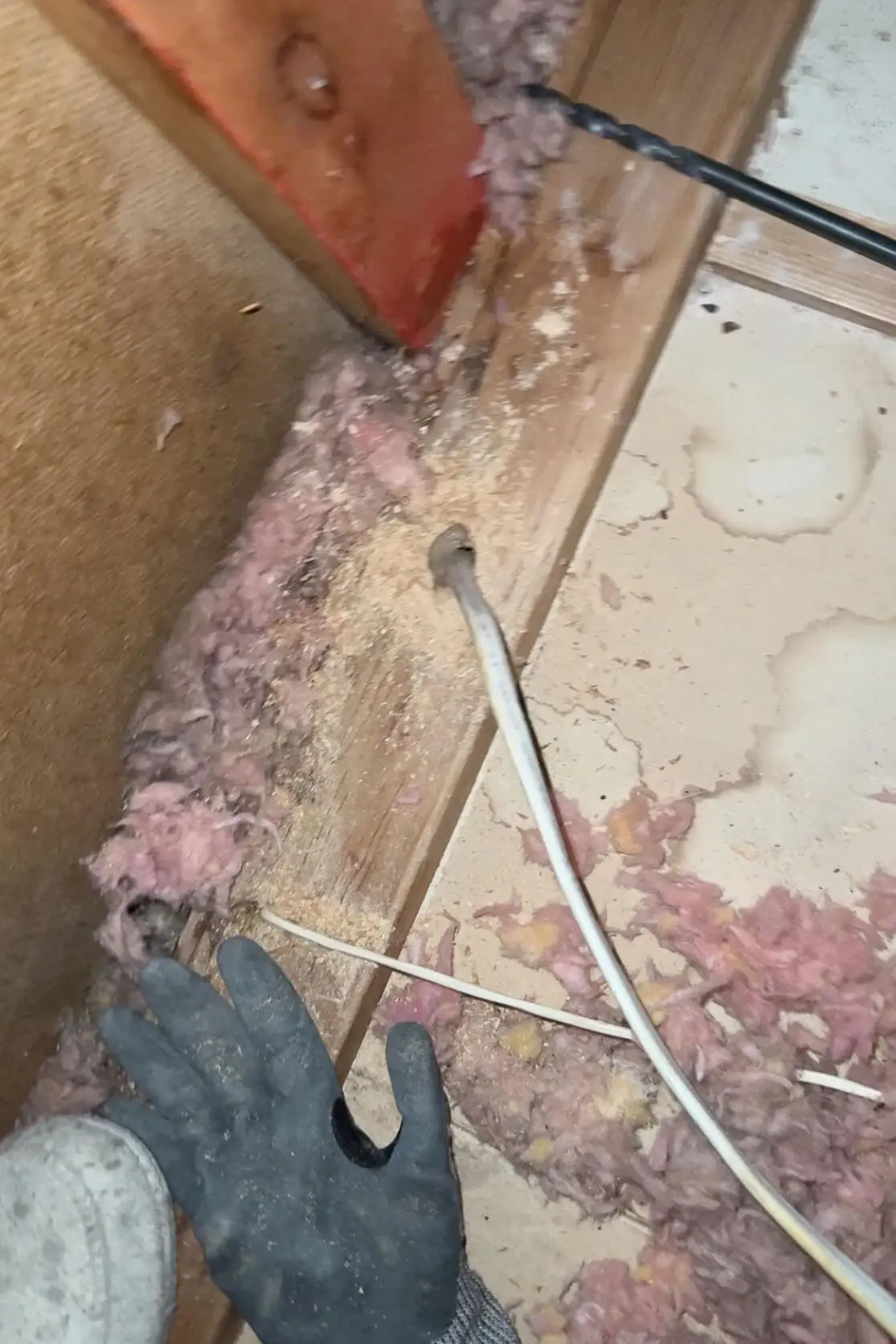 Close-up of a construction site showing a glove on the floor next to pink insulation material, wood shavings, and electrical wiring in a partially renovated space.